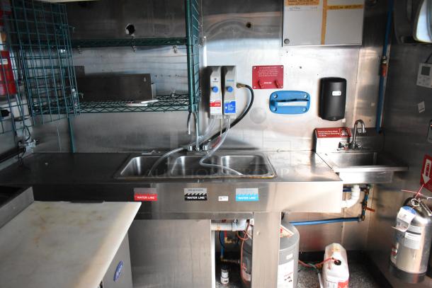 Fully equipped fast food trailer kitchen interior, featuring dual sinks, stainless steel surfaces, and a commercial water line setup.