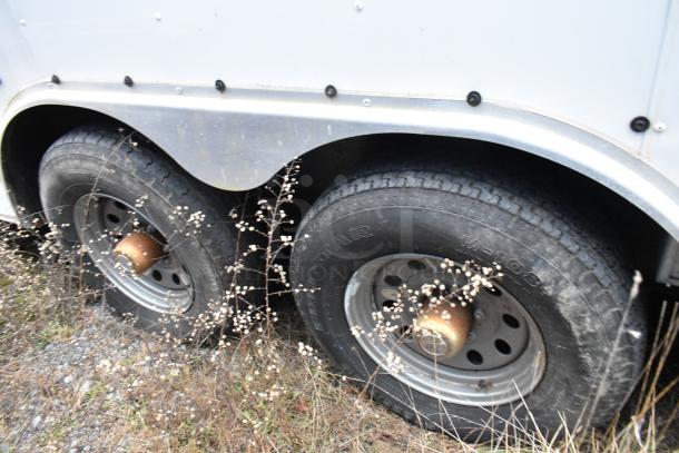 Close-up of dual tires on a Stuff4less 24' fast food trailer. Tires appear used with some dust and grass nearby.