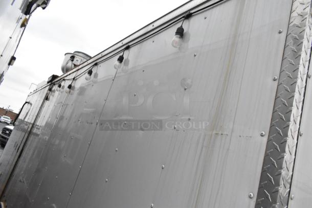 Side view of Stuff4less 24' mobile kitchen trailer, gray siding with exterior lights, fully equipped for fast food service.