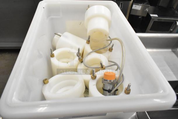 Assorted cookie machine parts in a white bin, including round components with bolts and wires, ready for auction.