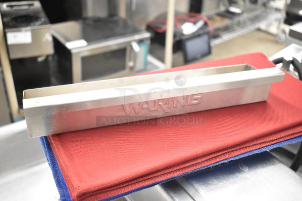 Waring panini press grease trap on a red cloth, showcasing the engraved Waring brand.