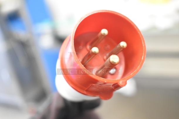 Red industrial electrical plug, possibly part of a Luohe Orange Floor Style Filling Machine, showing three brass prongs.