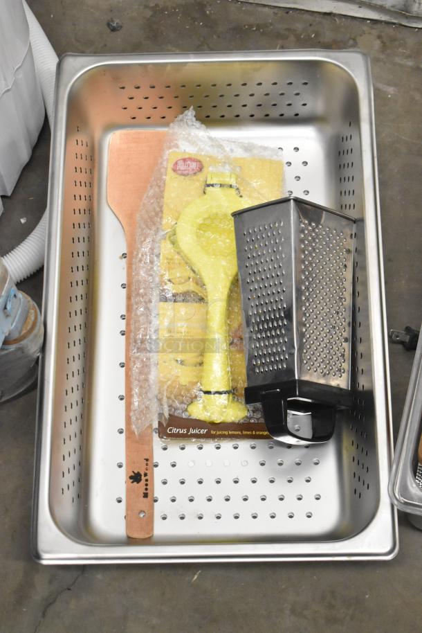 Lot of various items in metal perforated bin including bubble-wrapped yellow citrus juicer, metal grater, and wooden utensil.
