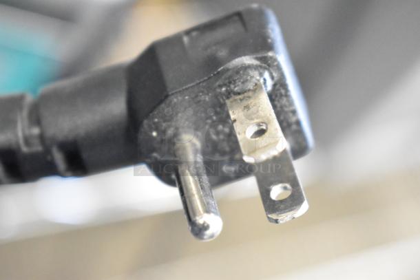 Close-up of a power plug for a 2019 Amana RCS10TS Commercial Microwave, showing prongs and black casing.