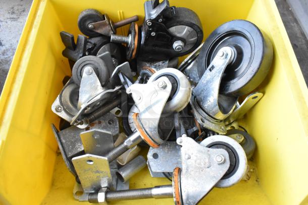 Lot of 20 commercial casters in a yellow bin, varying sizes, metal brackets, suitable for industrial use, good condition.