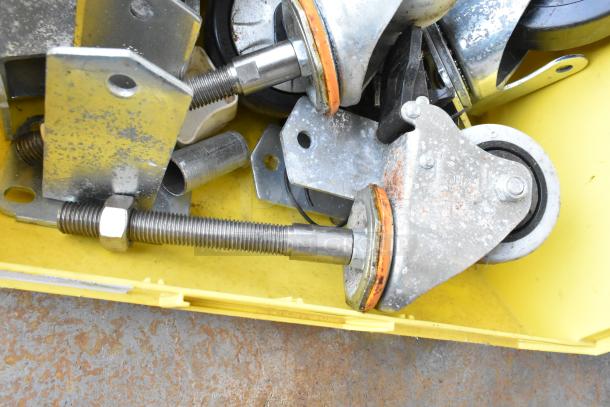 Lot of 20 items including metal commercial casters and hardware in a yellow bin, showing signs of wear.