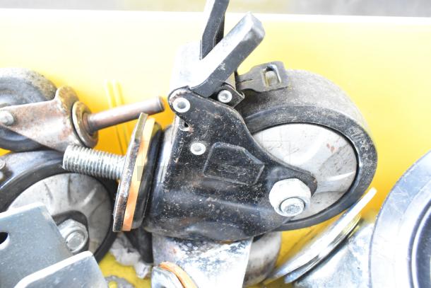 Lot of 20 various items including commercial casters in used condition, housed in a yellow bin. Some casters feature metal frames and visible wear.
