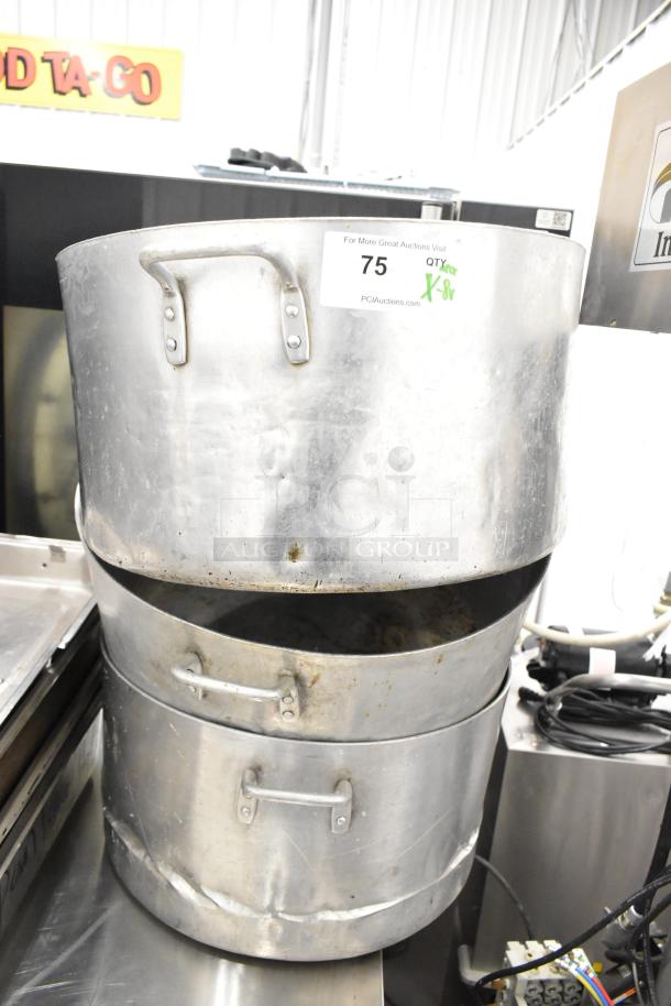 Stacked metal stock pots and bins, auction lot 75 with "8 times your bid" label, showing wear and dents.