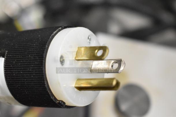 Close-up of a power plug for the Per-fil Micro-15 filler machine. Features brass prongs and a black grip.
