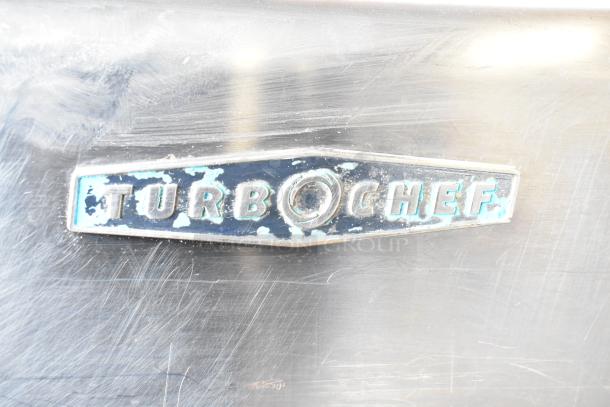 Turbochef HhC2020 logo on stainless steel commercial conveyor rapid cook oven. Visible wear on the emblem surface.