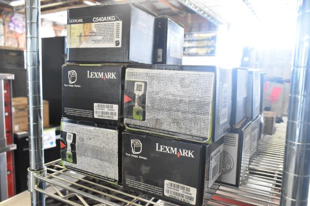 13 Lexmark ink cartridge boxes, model C540A1KG, on metal shelf, brand markings visible, condition unknown.