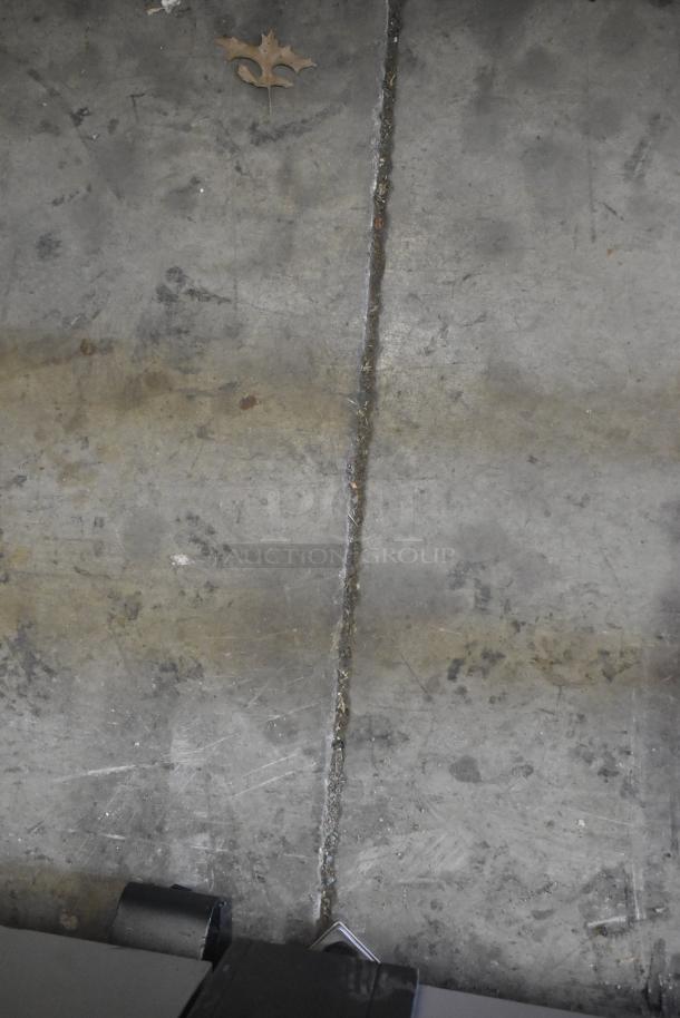 Image of concrete floor with a leaf, showing wear and a crack. No visible items or markings related to auction description.