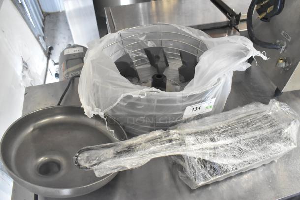 Three kitchen tools: citrus juicer guard, meat grinder tray, and taco shell fry basket, wrapped and marked with auction tag 134.