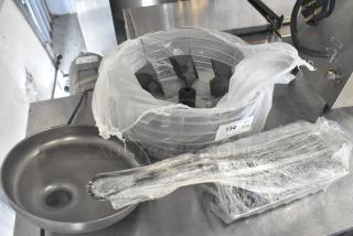 Three kitchen tools: citrus juicer guard, meat grinder tray, and taco shell fry basket, wrapped and marked with auction tag 134.