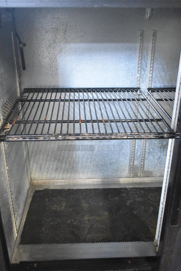 True TBB-24-48G-SD-S-LD back bar cooler interior, showcasing wire shelving, in worn but functional condition.