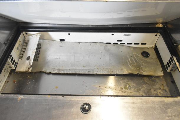 True TFP-48-18M-D-4 prep table interior, showing signs of wear. Features space for ingredients. Stainless steel surface.