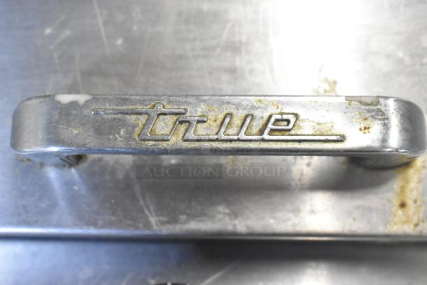 True brand logo on metal handle of TFP-48-18M-D-4 commercial prep table, showing signs of wear.