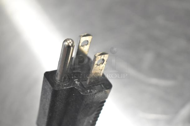 Close-up of a three-prong electrical plug viewed from above, with focus on metal prongs, set against a blurred background.