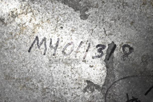 Close-up of handwritten black markings "M401319" on a textured gray surface.
