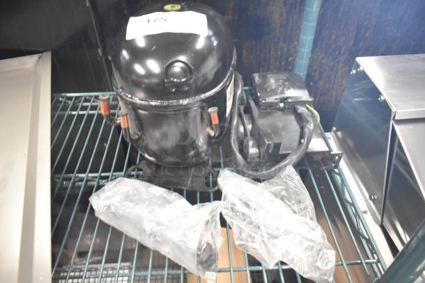 BRAND NEW Embraco NT6222UV Motor, 115V, 1 Phase, lightly scratched, visible labels, on metal shelf.