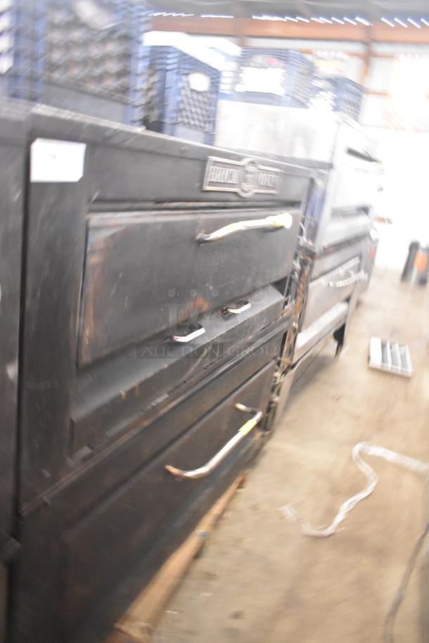 Two commercial single deck pizza ovens, dark finish, visible wear, "BRICK OVEN" label, sturdy handles, industrial use.