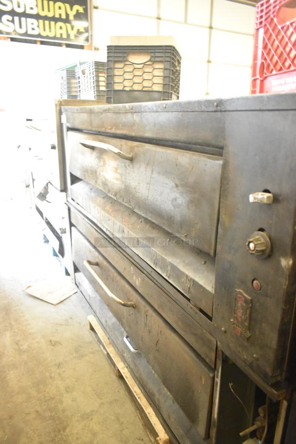 Two commercial single-deck pizza ovens, metal exterior, used condition, temperature knobs visible, stacked crates nearby.