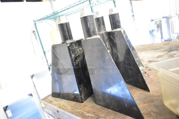 Four black metal objects on a shelf, possibly components or attachments, with visible signs of wear.