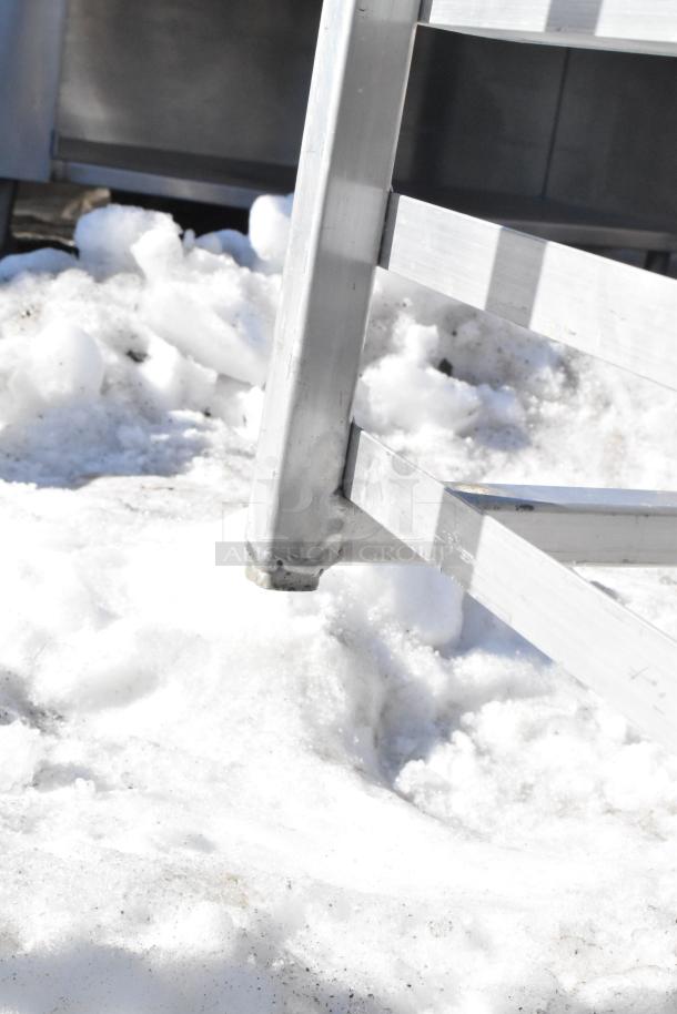 Commercial pan transport rack with durable aluminum frame on snow, featuring sturdy commercial casters.