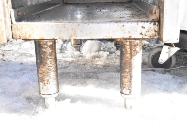 Commercial drain board with 2 under shelves and wheels, showing signs of rust and wear. Suitable for heavy-duty use.