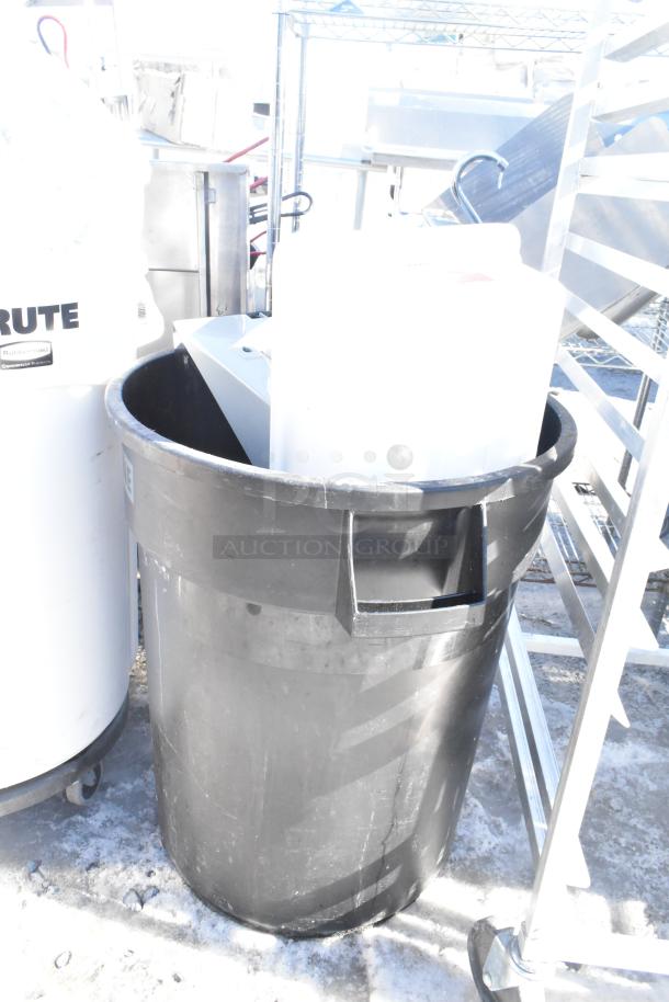 Two poly trash cans, one black, one white, with assorted contents. Visible label on white can: Rubbermaid Brute.