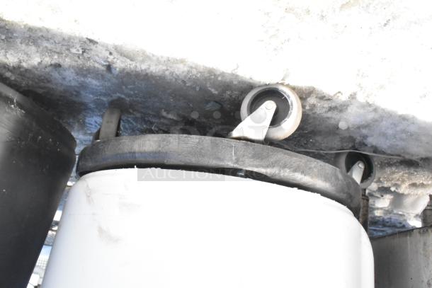 Two poly trash cans with roller wheels, black and white, containing unspecified contents, in used condition.