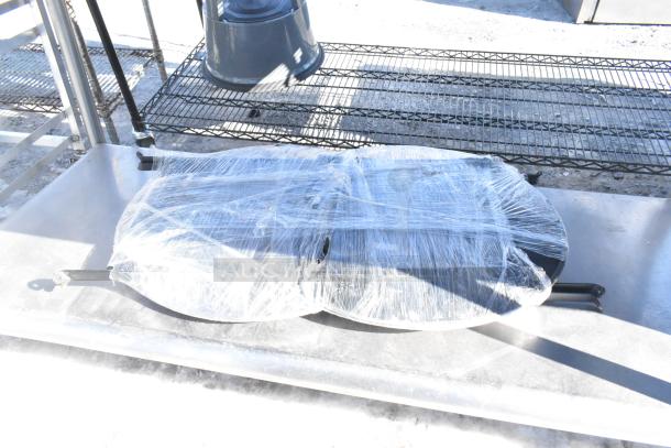 Commercial table with under shelf, wrapped in plastic for protection, metal construction, suitable for heavy-duty use.