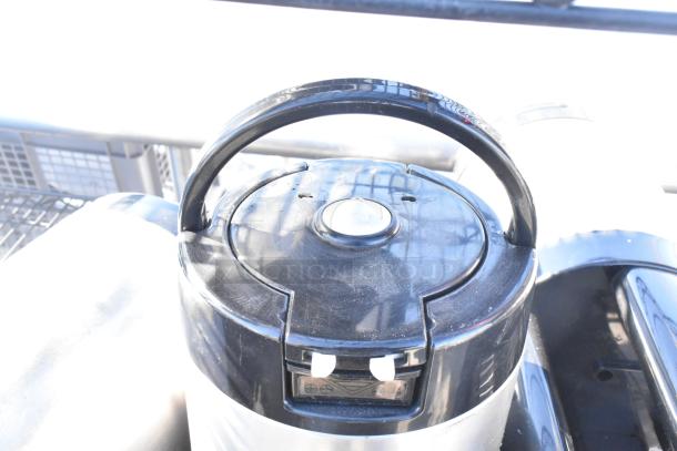 A close-up of a black handle on top of a shiny, metallic container. Visible plastic components and shadow details.