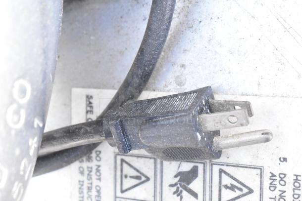 A close-up of a black electrical plug next to a safety warning label.