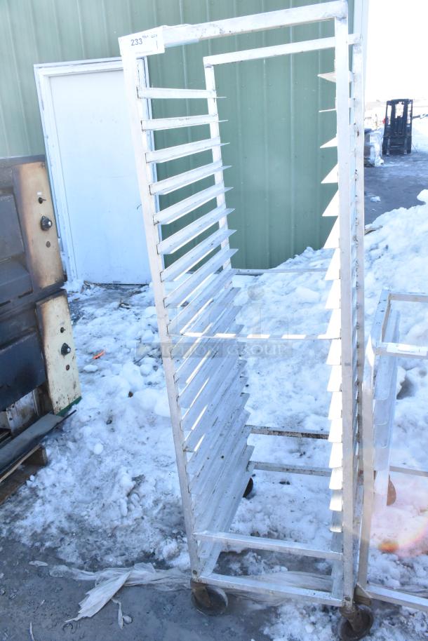 Commercial pan transport rack on casters with multiple slots, outdoor setting, used condition, tag number 233 visible.