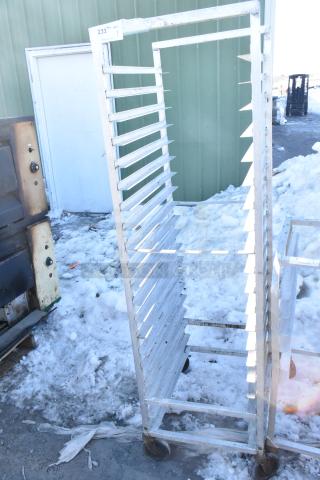 Commercial pan transport rack on casters with multiple slots, outdoor setting, used condition, tag number 233 visible.