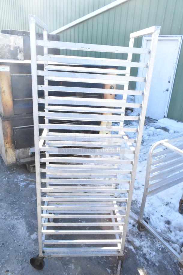 Commercial pan transport rack with multiple shelves on durable commercial casters, showing signs of use outdoors.