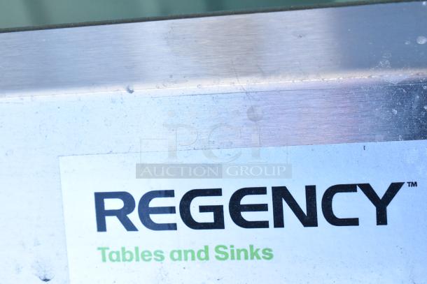 Brand new, scratch and dent Regency 600S31818218 stainless steel three-compartment sink, 16 gauge, with cross bracing and two 18" drainboards. Tag reads "REGNECY Tables and Sinks".