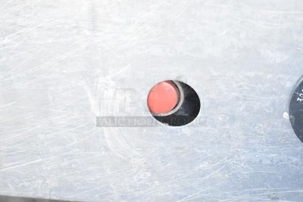 Close-up of a red button on a Montague commercial pizza oven panel, showing stainless steel surface with light scratches.
