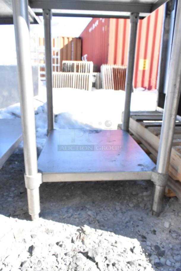 Commercial metal table with under shelf, sturdy legs, outdoor setting. Ideal for industrial use. Minor wear visible.