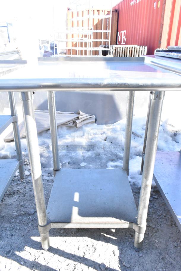 Commercial table with under shelf, stainless steel, showing some wear. Ideal for kitchen or workshop use.