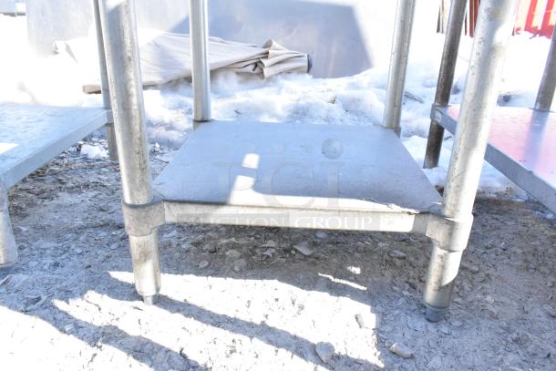 Commercial metal table with under shelf, durable legs, signs of wear, suitable for heavy-duty use in industrial settings.