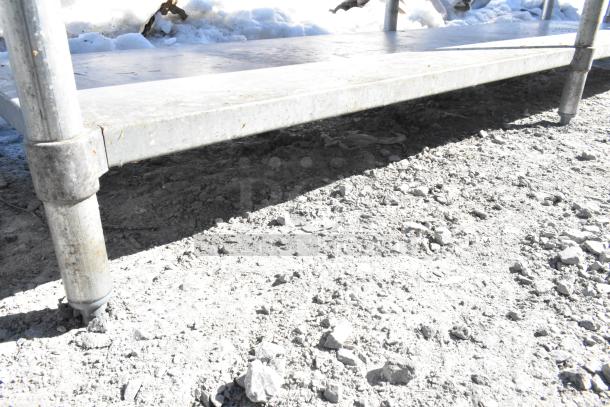 Commercial metal table with two undershelves. Sturdy construction with visible wear. Ideal for storage or industrial use.