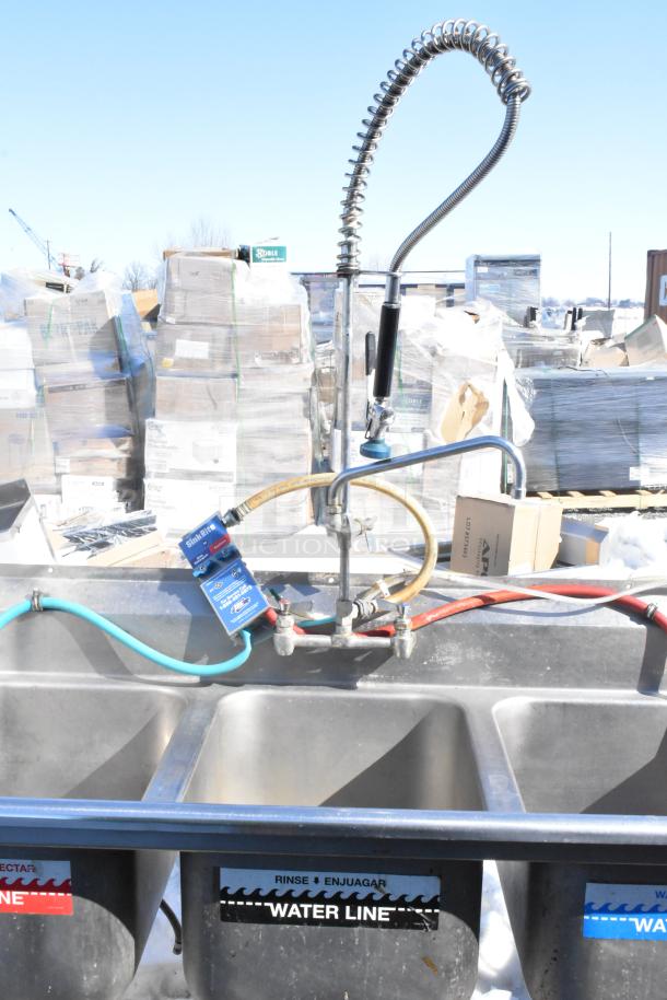 Commercial 3 bay sink with dual drain boards, faucet, handles, and spray nozzle attachment. Rinse and water line labels visible.