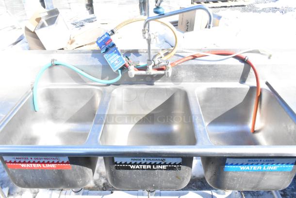 Commercial 3 bay sink with dual drain boards, faucet, handles, and spray nozzle attachment. Features labeled water lines.