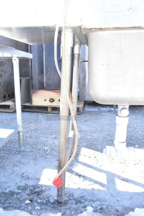 Commercial 3-bay sink with dual drain boards, faucet, handles, and spray nozzle attachment. Visible wear on surfaces.