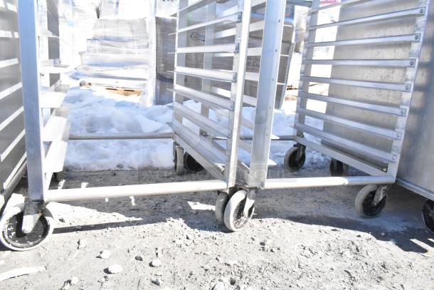 2 commercial pan transport racks on casters, metal construction, multiple shelves, outdoor setting, good condition.
