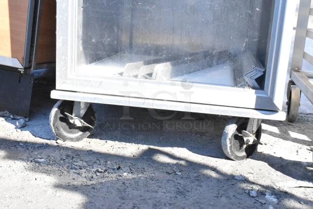 Lockwood enclosed pan transport rack on commercial casters, showing wear; ideal for transporting baked goods securely.