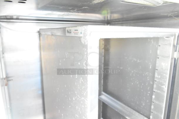 Commercial Single Door Reach In Cooler, stainless steel interior, visible shelving brackets, manufacturer label inside.