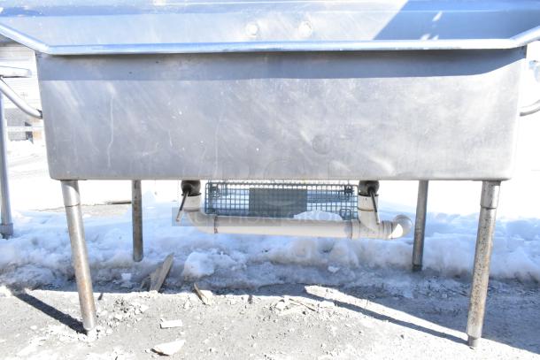 Commercial 2 bay stainless steel sink with dual drain boards, visible wear on legs, suitable for high-capacity usage.